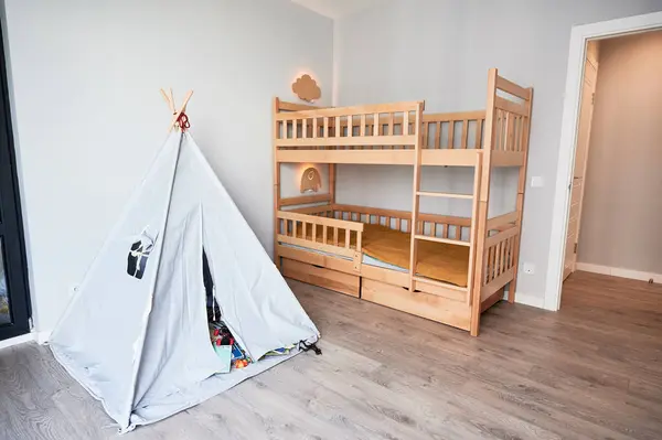 Kid room with wooden bunk bed, wigwam and elegant minimalist interior design in apartment after renovation. Child bedroom with comfortable kid bed, laminate floor, white walls and open door.