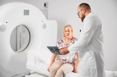 Tıbbi bilgisayarlı tomografi ya da MRI tarayıcısı. Doktor MRI sonuçlarını tutuyor ve açıklıyor. MRI 'dan sonra kadın hasta, kanepede oturuyor. Tıp, sağlık ve modern teşhis kavramı.