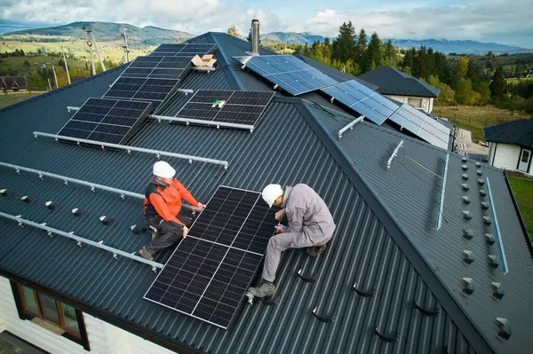 在房顶上安装光电太阳能电池板的技师 头盔上的男性工程师使用六角钥匙建造太阳能组件系统 可再生能源的替代概念 图库照片