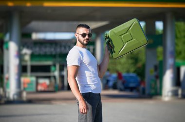 Tüplü kendine güvenen adam sonunda benzin istasyonunu buldu. Benzin istasyonunun arka planında boş bir teneke kutuyla genç bir erkeğin portresi..