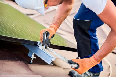 Fotovoltaik etkilerle elektrik üretmek için evin çatısına güneş paneli inşa eden işçiler. Montaj ekipmanlarını ölçmek için cetvel kullanan adamı kapat.