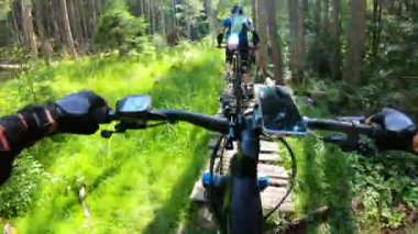Bakış açısı. Ormanda elektrikli dağ bisikleti süren iki bisikletçi. Bisiklet gidonundaki akıllı telefon. Macera kavramı, dışarıda boş zaman geçirmek..