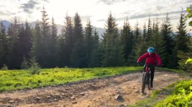 Dışarıda elektrikli dağ bisikleti süren bisikletçi. Erkek turist dağlarda otlak patika boyunca bisiklet sürüyor, başlık ve sırt çantası takıyor. Spor anlayışı, aktif eğlence ve doğa.