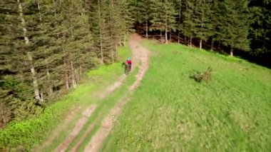 Dışarıda elektrikli dağ bisikleti süren bisikletçi. Erkek turistin dağlardaki otlak patika boyunca bisiklet sürüşünü, kaskını ve sırt çantasını gösteren hava manzarası. Spor anlayışı, aktif eğlence ve doğa.