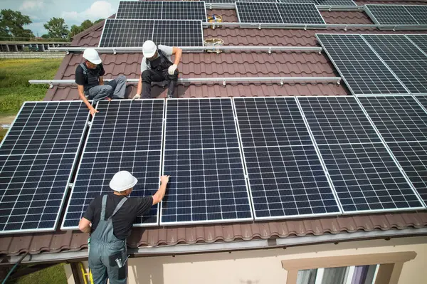 stock image Men workers installing photovoltaic solar moduls on roof of house. Engineers in helmet building solar panel system outdoors. Concept of alternative and renewable energy. Aerial view.