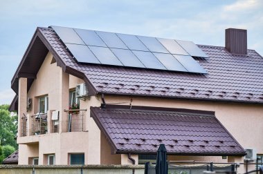 Çatıda fotovoltaik etkiyle elektrik üretmek için güneş panelleri olan bir ev. Çatıda güneş enerjisi sistemi olan bir ev. Alternatif enerji kavramı, özerklik, güç sürdürülebilir kaynaklar.