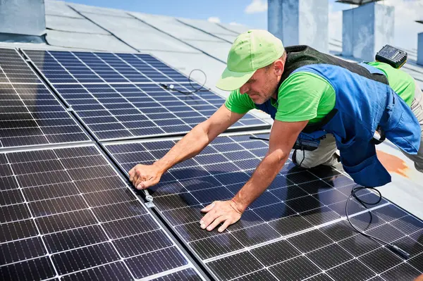Worker building photovoltaic solar panel system on rooftop of house. Close up of man engineer installing solar module with help of wrench outdoors. Alternative and renewable energy generation concept.