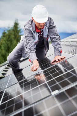 Elektrikçi adam evin çatısına fotovoltaik güneş panelleri monte ediyor. Başlıktaki mühendis, uğursuz anahtarın yardımıyla güneş modülü sistemi kuruyor. Alternatif, yenilenebilir enerji kavramı.