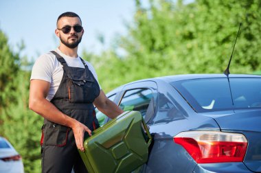 Profesyonel işçinin benzinle doldurduğu bozuk bir araba. Benzin deposuna benzin dolduran genç bir adamın portresi. Mavi arabalı, tulumlu ve güneş gözlüklü bir erkek işçi..