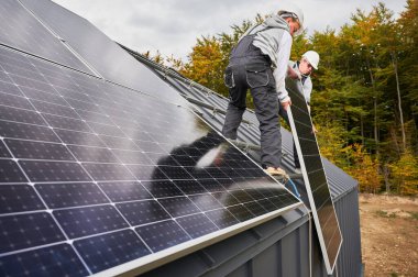 Elektrikçiler evin çatısına güneş paneli kuruyor. Miğferli işçiler fotovoltaik güneş modülünü dışarı halatların yardımıyla kaldırıyorlar. Alternatif ve yenilenebilir enerji kavramı.
