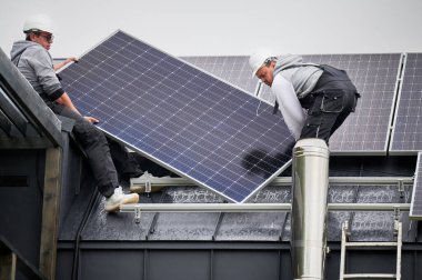 Evin çatısına güneş paneli inşa eden mühendisler. Dışarıda fotovoltaik güneş modülü taşıyan miğferli işçiler. Alternatif ve yenilenebilir enerji kavramı.