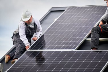 Elektrikçiler evin çatısına fotovoltaik güneş modülü istasyonu inşa ediyorlar. Miğferli teknisyenler güneş paneli sistemi kuruyor. Alternatif ve yenilenebilir enerji kavramı.