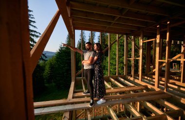 Ormanın yakınındaki dağlarda yuva yapmış gelecekteki ahşap iskelet evlerini araştıran kadın ve erkek. Sabahın erken saatlerinde şantiyedeki genç çift. Çağdaş ekolojik yapı kavramı.