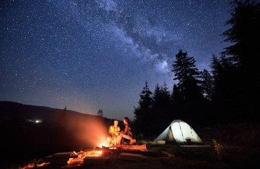 Parıldayan yıldızların altında gece vakti kamp yapmak. Erkek ve kadın, hevesli gezginler, kamp ateşiyle gençleşiyorlar, sakin ormanın ortasında, büyülü gece gökyüzünün altında çadır kuruyorlar..