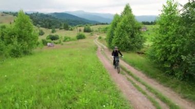 Dışarıda elektrikli dağ bisikleti süren bisikletçi. Erkek turistin dağlardaki otlak patika boyunca bisiklet sürüşünü, kaskını ve sırt çantasını gösteren hava manzarası. Spor anlayışı, aktif eğlence ve doğa.