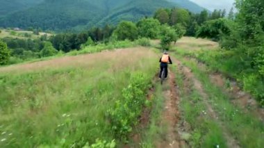 Dışarıda elektrikli dağ bisikleti süren bisikletçi. Turistlerin dağlardaki otlak patika boyunca bisiklet sürüşlerinin kaskı ve sırt çantasıyla hava manzarası. Spor anlayışı, aktif eğlence ve doğa.