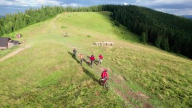 Dışarıda elektrikli bisiklet süren bir grup bisikletçi. Erkek turistlerin yazın dağlarda çimenli patikada bisiklet sürüşlerini gösteren hava manzarası. Spor anlayışı, aktif eğlence ve doğa.