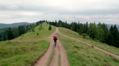 Dışarıda elektrikli dağ bisikleti süren bisikletçi. Turistlerin dağlardaki otlak patika boyunca bisiklet sürüşlerinin kaskı ve sırt çantasıyla hava manzarası. Spor anlayışı, aktif eğlence ve doğa.
