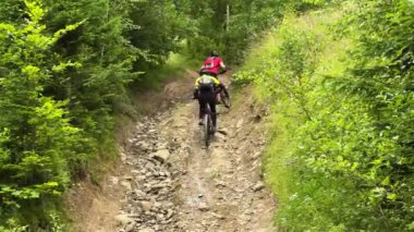 Dışarıda bisiklete binen iki bisikletçi. Erkek turistler dağlarda bisiklet sürüyorlar, kaskları ve sırt çantaları takıyorlar. Spor anlayışı, aktif eğlence ve doğa.