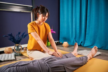 Masör Tayland yogası masajı yapıyor. Kadın terapist erkek hasta için evde geleneksel masaj tedavisi uyguluyor. Müşteri paspasın üzerinde uzanıyor, meditasyon yapıyor, sakin bir atmosferde el masajının keyfini çıkarıyor..