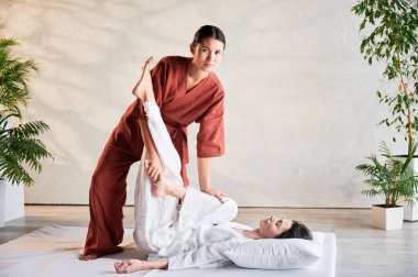 Masör Tayland yogası masajı yapıyor. Geleneksel masaj tedavisi uygulayan kadın terapist, kadın hastaların vücudunu geriyor. Müşteri paspasın üzerinde uzanıyor, sakin atmosferde el masajının keyfini çıkarıyor..