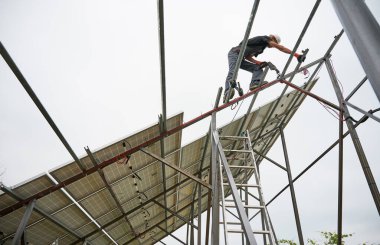 Metal rayların üzerinde duran ve fotovoltaik güneş panelleri için destek yapısını kurarken elektrikli matkap kullanan insan mühendisi. Beyaz arkaplanda izole.