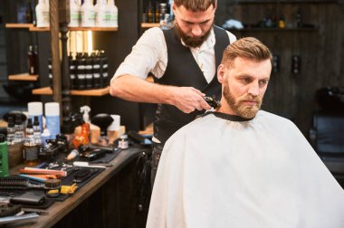 Profesyonel berber müşterinin ensesini tıraş ediyor. Sakallı yakışıklı müşteri şık saç tıraşı oluyor. Kendine güveni tam bir adam berber dükkanına düzenli olarak gelir..