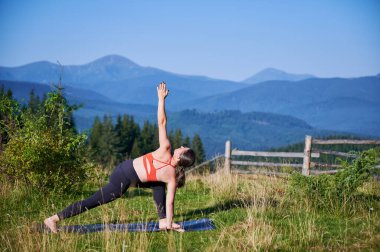 Dağlarda yoga yapan bir kadın, sakin, doğal bir ortamda. Kadın yoga pozu veriyor paspasın üzerinde, gün doğumunda ya da günbatımında güzel dağ manzarasının arka planıyla.