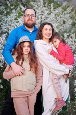 Aile alerjisi, bahardaki mevsimsel alerjiden kaynaklanan tedaviden sonra tadını çıkarıyor. Mutlu anne, baba ve iki kız baharda çiçek ağaçlarının önünde gülümsüyorlar. Bahar alerjisi konsepti.