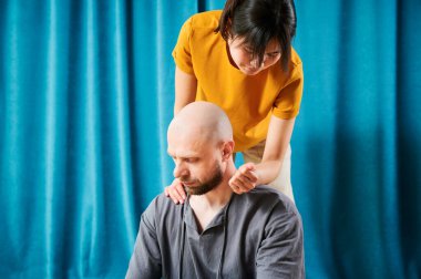 Masseuse making thai yoga massage. Woman therapist doing traditional massage treatment for male patient indoors. Close up view of bald client meditating, enjoying hand massage in calm atmosphere.