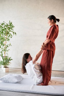 Masör Tayland yogası masajı yapıyor. Geleneksel masaj tedavisi uygulayan kadın terapist, kadın hastaların vücudunu geriyor. Müşteri paspasın üzerinde uzanıyor, sakin atmosferde el masajının keyfini çıkarıyor..