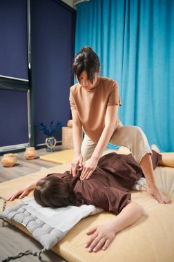 Masör Tayland yogası masajı yapıyor. Kadın terapist, kadın hasta için evde geleneksel masaj tedavisi uyguluyor. Müşteri paspasın üzerinde uzanıyor, meditasyon yapıyor, sakin bir atmosferde el masajının keyfini çıkarıyor..