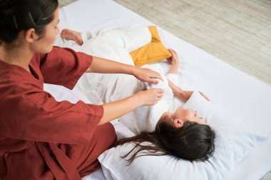 Masör Tayland yogası masajı yapıyor. Kadın hasta için geleneksel masaj tedavisi uygulayan kadın terapist. Müşteri paspasın üzerinde uzanıyor, meditasyon yapıyor, sakin bir atmosferde el masajının keyfini çıkarıyor. Kırpılmış görünüm.