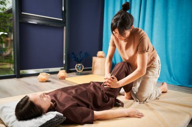 Masör Tayland yogası masajı yapıyor. Kadın terapist, kadın hasta için evde geleneksel masaj tedavisi uyguluyor. Müşteri paspasın üzerinde uzanıyor, meditasyon yapıyor, sakin bir atmosferde el masajının keyfini çıkarıyor..