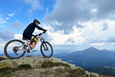 Dışarıda elektrikli dağ bisikleti süren bisikletçi. Erkek turist dağlarda otlak patika boyunca bisiklet sürüyor, başlık takıyor. Spor anlayışı, aktif eğlence ve doğa.