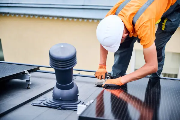 stock image Worker building photovoltaic solar panel system on rooftop of house. Man engineer in helmets and gloves installing solar module with help of hex key outdoors. Renewable energy generation concept.