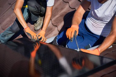 İşçiler evin çatısına güneş paneli inşa ediyorlar. İki adam dışarı fotovoltaik güneş modülü kuruyor. Alternatif, yeşil ve yenilenebilir enerji üretimi kavramı.