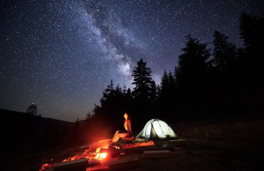 Gece kamp macerası dağlarda, parıldayan yıldızların altında. Dişi gezgin şenlik ateşiyle dinleniyor ve çadırı ormanın yakınında, gökyüzünün altında Chumack Patikası 'nın görkemli güzelliğiyle süsleniyor..