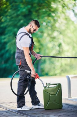 Profesyonel işçi yakıt bidonu dolduruyor. Müşteri için sarnıca benzin dolduran yetenekli bir adam. Benzin deposunun yanında pompa başlıklı bir adam yakıt deposu dolduruyor..