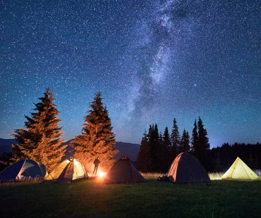 Yıldızlı gökyüzünün altındaki dağlarda gece kampı. Kamp alanlarında dinlenen turist silueti, yıldızlı ve Samanyolu 'nun altında yanan kamp ateşi. Turizm kavramı, doğanın güzelliği..