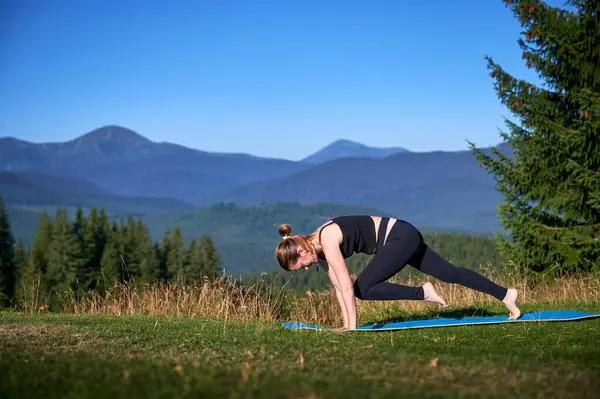 Dağlarda yoga yapan bir kadın, sakin, doğal bir ortamda. Kadın yoga pozu veriyor paspasın üzerinde, gün doğumunda ya da günbatımında güzel dağ manzarasının arka planıyla.