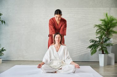 Masör Tayland yogası masajı yapıyor. Kadın terapist, kadın hasta için evde geleneksel masaj tedavisi uyguluyor. Müşteri mindere oturuyor, meditasyon yapıyor, sakin bir atmosferde el masajının keyfini çıkarıyor..