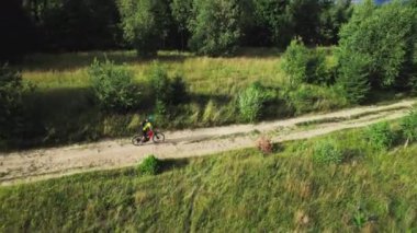 Dışarıda elektrikli dağ bisikleti süren bisikletçi. Erkek turistin dağlardaki otlak patika boyunca bisiklet sürüşünü, kaskını ve sırt çantasını gösteren hava manzarası. Spor anlayışı, aktif eğlence ve doğa.