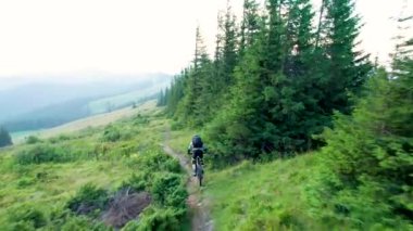 Dışarıda elektrikli dağ bisikleti süren bisikletçi. Erkek turistin dağlardaki otlak patika boyunca bisiklet sürüşünü, kaskını ve sırt çantasını gösteren hava manzarası. Spor anlayışı, aktif eğlence ve doğa.