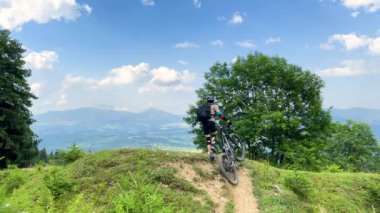 Dışarıda elektrikli dağ bisikleti süren bisikletçi. Erkek turist dağlarda otlak patika boyunca bisiklet sürüyor, başlık ve sırt çantası takıyor. Spor anlayışı, aktif eğlence ve doğa.