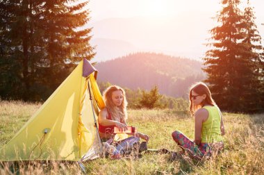 Dışarıda kamp yapan iki kadın yürüyüşçü. Kamp alanında oturan genç kadınlar, mola veriyorlar. Arkadaşlar çimenlerde oturur, konuşur, su döker, çay yaparlar. Turizm ve dağlarda yürüyüş kavramı.