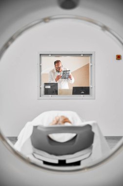 Tıbbi bilgisayarlı tomografi ya da MRI tarayıcısı. MR 'ı inceleyen doktor klinikte sonuç verir. Gözlüklü ve üniformalı bir erkek uzman, tarama yapıyor, çalışıyor. Tıp ve hastane kavramları.