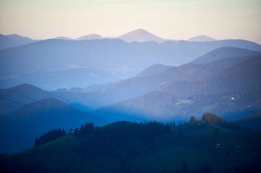 Mavi ve yeşilin gölgelerinde yuvarlanan dağların sakin manzarası, yumuşak, pastel gökyüzünün altında uzak tepeler, huzurlu ve huzurlu bir manzara yaratıyor..