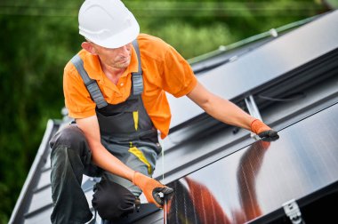 Evin çatısına güneş paneli inşa eden bir işçi. Dışarıda fotovoltaik güneş modülü kuran miğferdeki adam mühendis. Alternatif, yeşil ve yenilenebilir enerji üretimi kavramı.