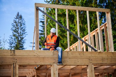 Marangoz ormanın yakınında iki katlı ahşap çerçeve inşa ediyor. Sakallı adam binaya çivi çakıyor koruyucu kask takıyor, çelik yelek giyiyor. Modern ekolojik yapı kavramı